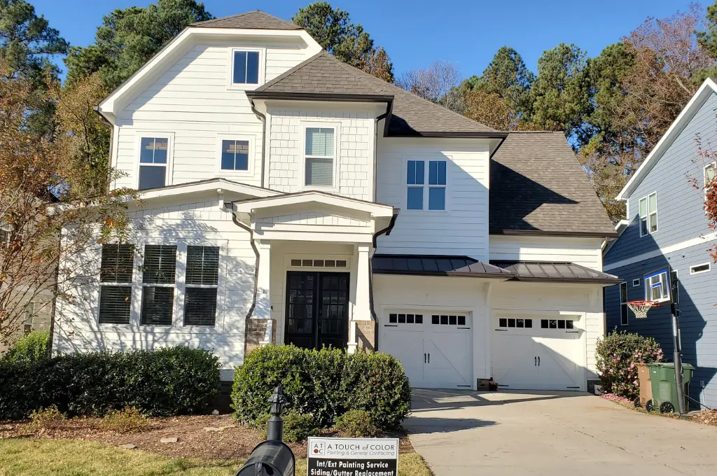 The front of a monochromatic white home exterior in Cary, NC, with bronze gutters, all costs and service by A Touch of Color.