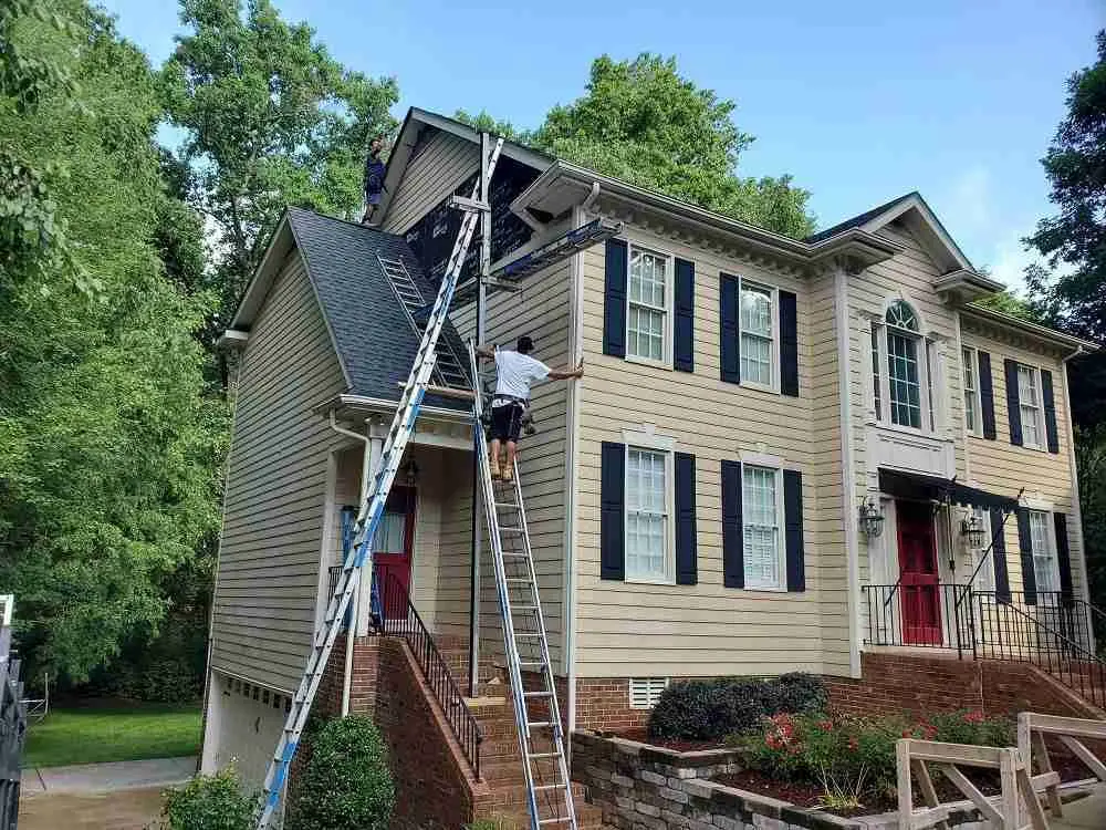 A Touch of Color workers set up for siding work on a large home's roofline.