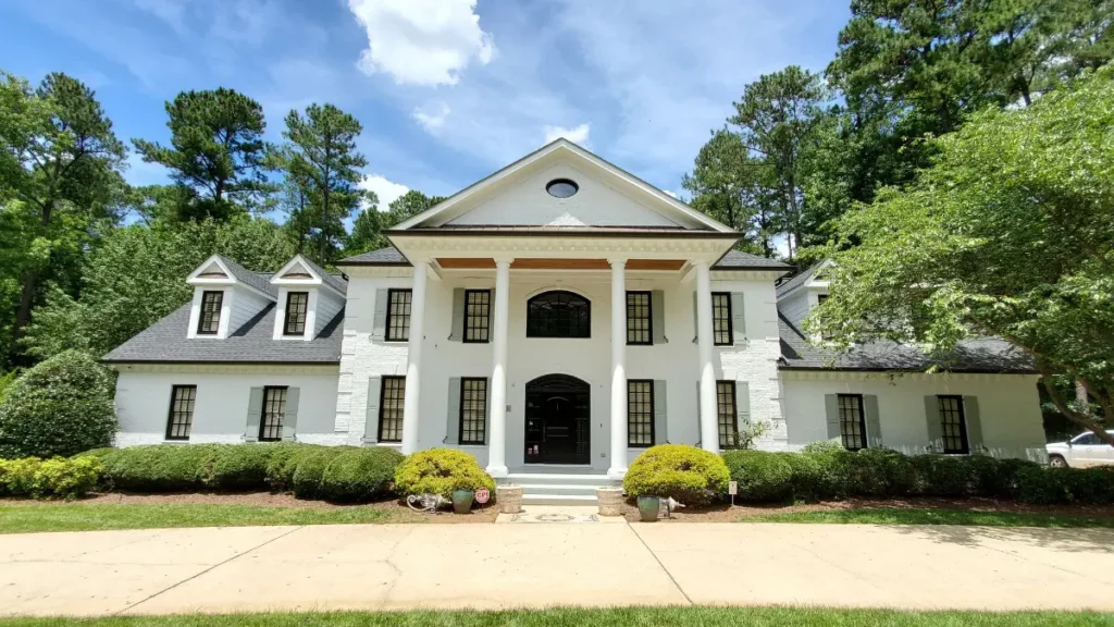 Exterior painting of a large white brick house in Wake Forest, NC, featuring a crisp white finish with modern black windows and new custom shutters.