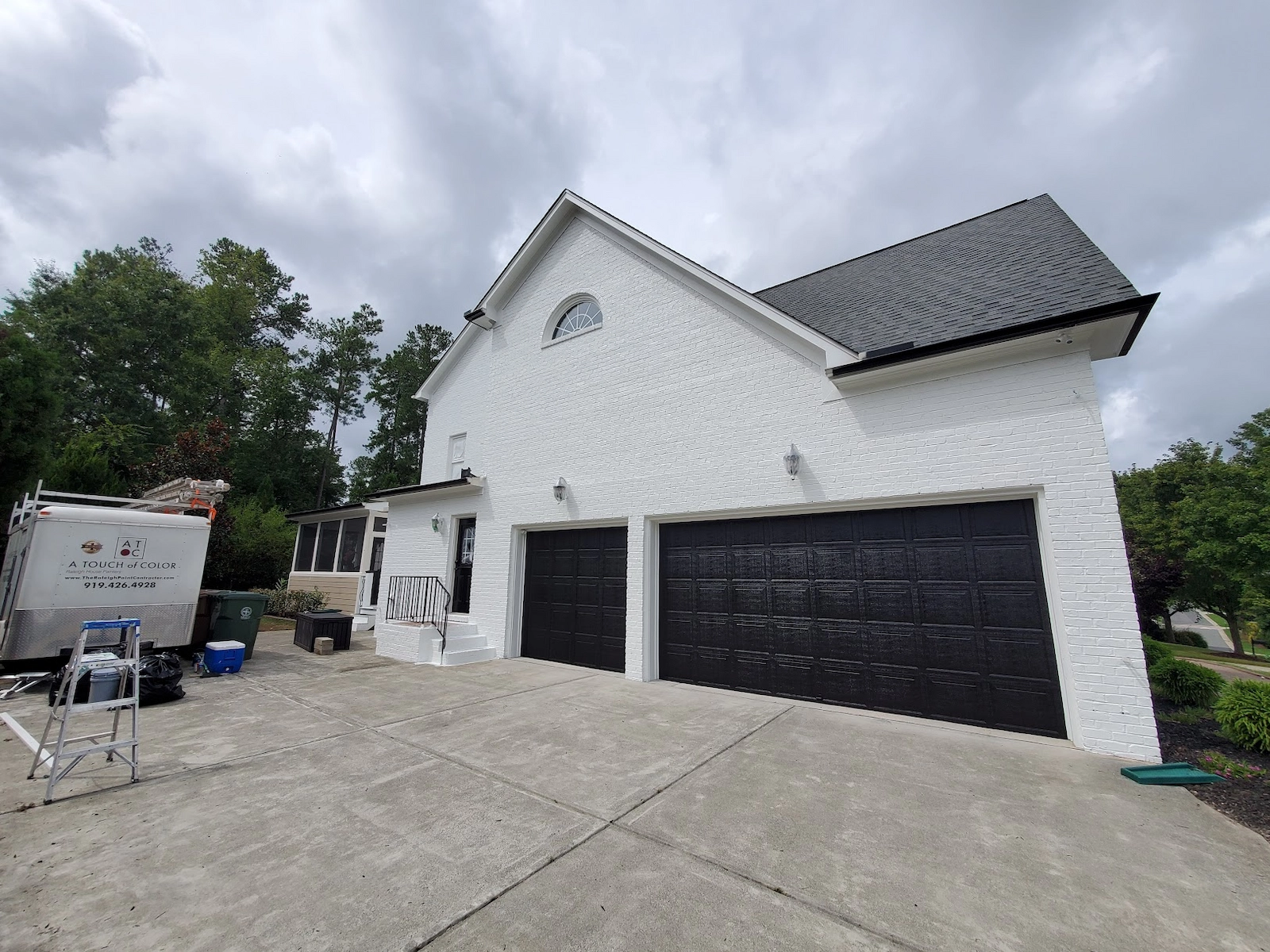 Professional exterior brick painting in Cary, NC, featuring a high-durability white masonry coating and high-contrast black shutters, with a branded A Touch of Color trailer on-site to ensure a technical, high-performance finish.